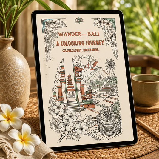 A framed art print featuring a Bali-themed coloring book cover titled 'WANDER - BALI A COLOURING JOURNEY' displayed on a woven mat next to a ceramic vase with plumeria flowers and a cup.